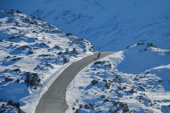 a couple of people are walking down a snowy mountain road .