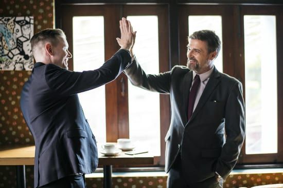 two men in suits are giving each other a high five .