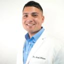 a man wearing a white lab coat and a blue shirt is smiling for the camera .