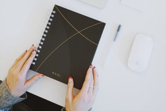 a woman is holding a black spiral notebook in her hands .