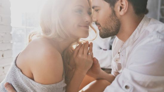 a man and a woman are touching noses and holding hands . the woman is wearing a ring on her finger .