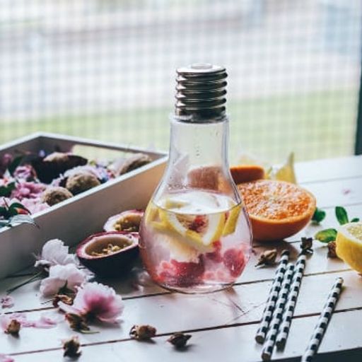 a light bulb shaped bottle filled with water and fruit on a table .