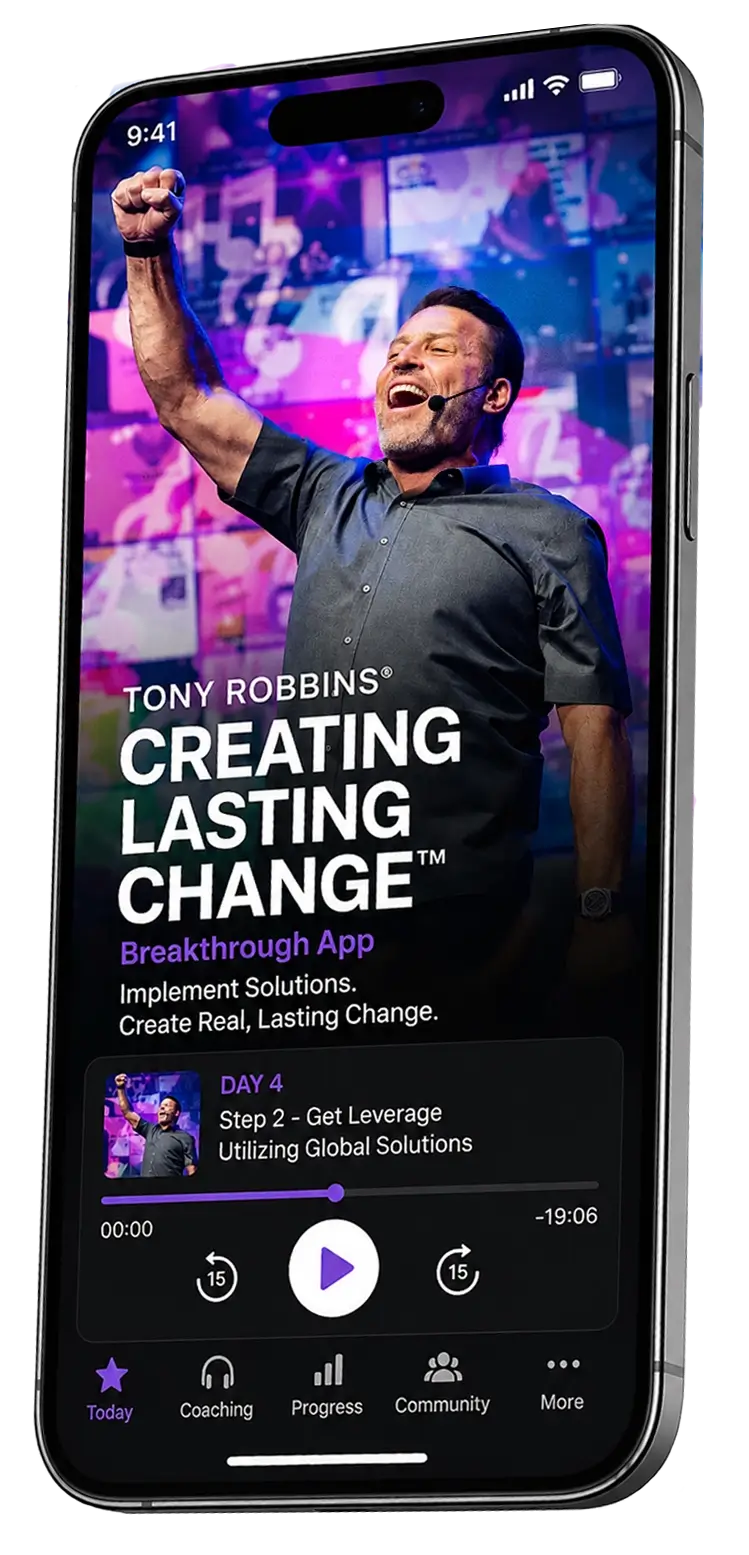 A smartphone displays the Tony Robbins "Creating Lasting Change Breakthrough App," featuring Tony Robbins raising a fist on a video screen.