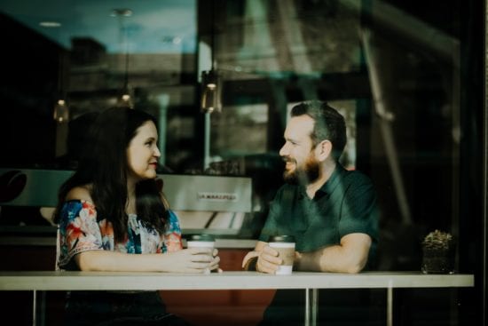 a man and a woman are sitting at a table in a cafe talking to each other .