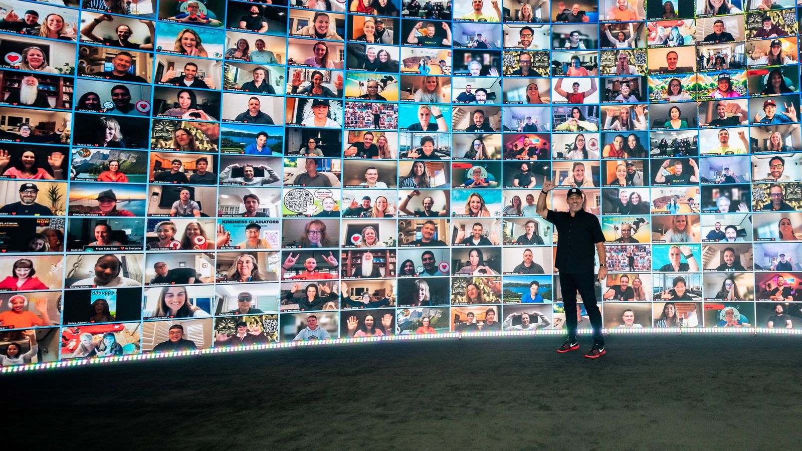 a man is standing in front of a wall filled with lots of pictures of people .