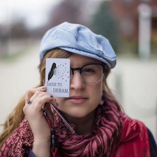 a woman wearing glasses and a hat is holding a piece of paper in front of her eye .