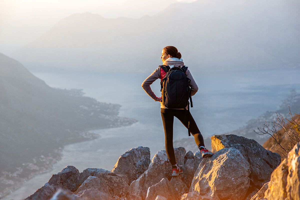 a woman with a backpack is standing on top of a rocky mountain .