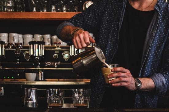 a man is pouring milk into a cup of coffee .