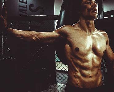 a shirtless man is standing in a gym with his arms outstretched .