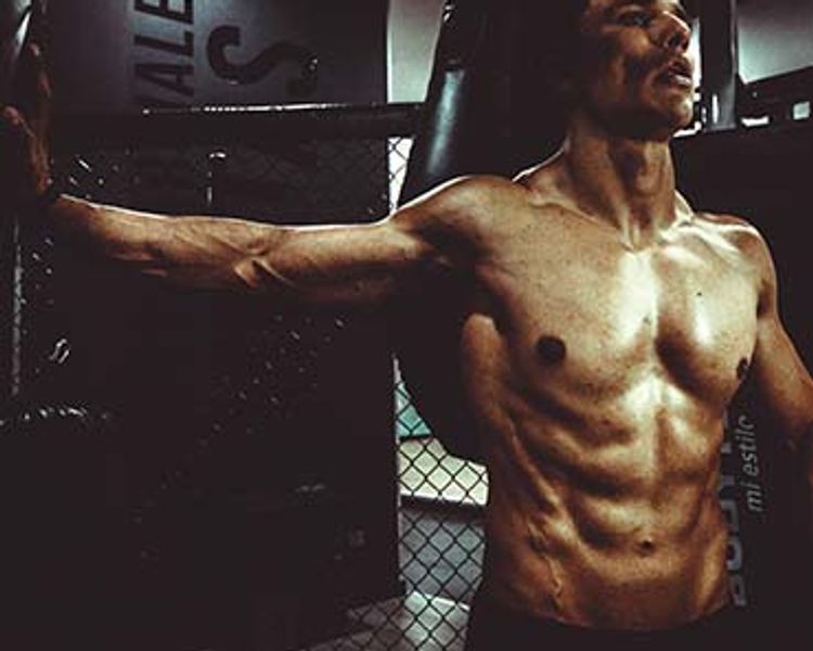 a shirtless man is standing in a gym with his arms outstretched .