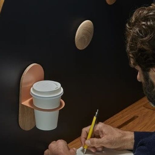 a man is writing on a piece of paper next to a coffee cup holder .