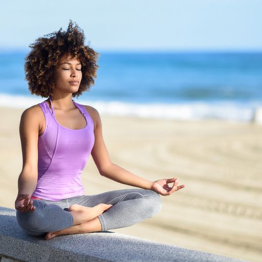 a woman is sitting in a lotus position on the beach with her eyes closed .