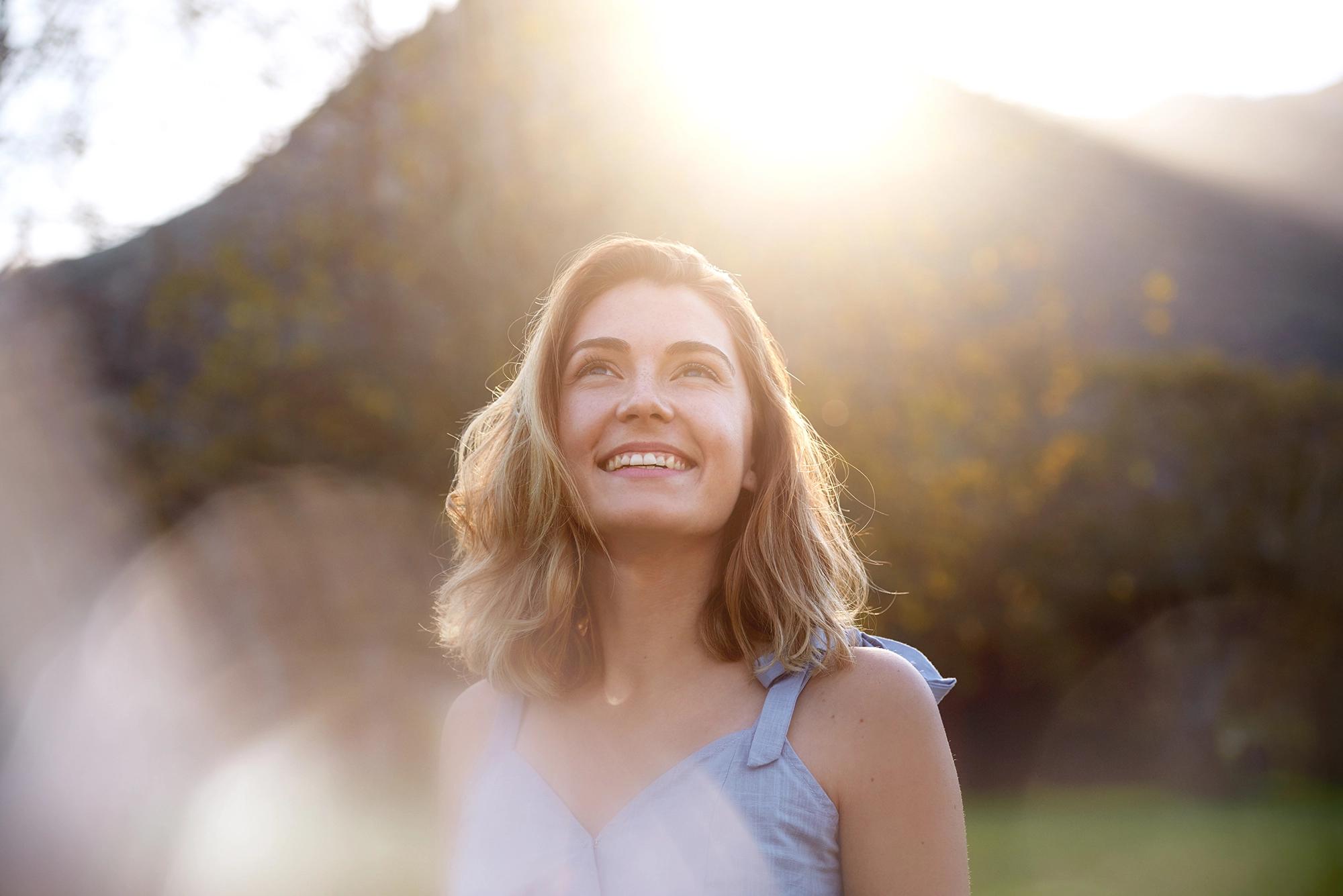 Smiling woman looking up into bright sunlight with a blurred natural background.