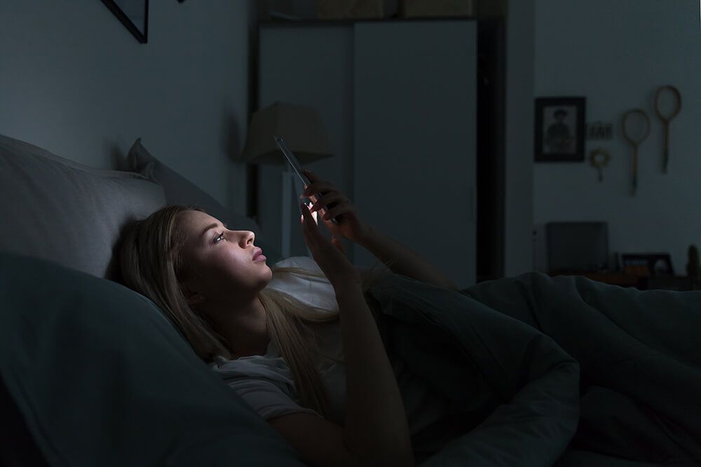 a woman is laying in bed at night looking at her cell phone .
