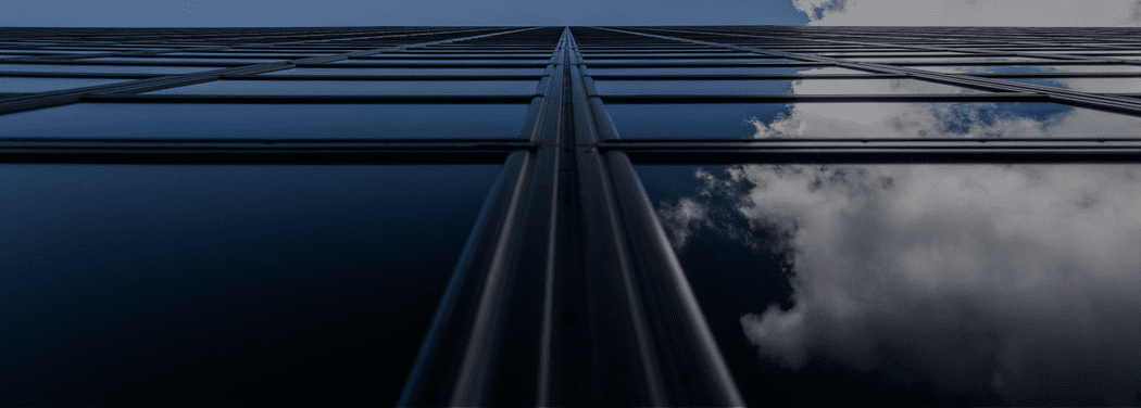 looking up at a tall building with clouds reflected in the windows