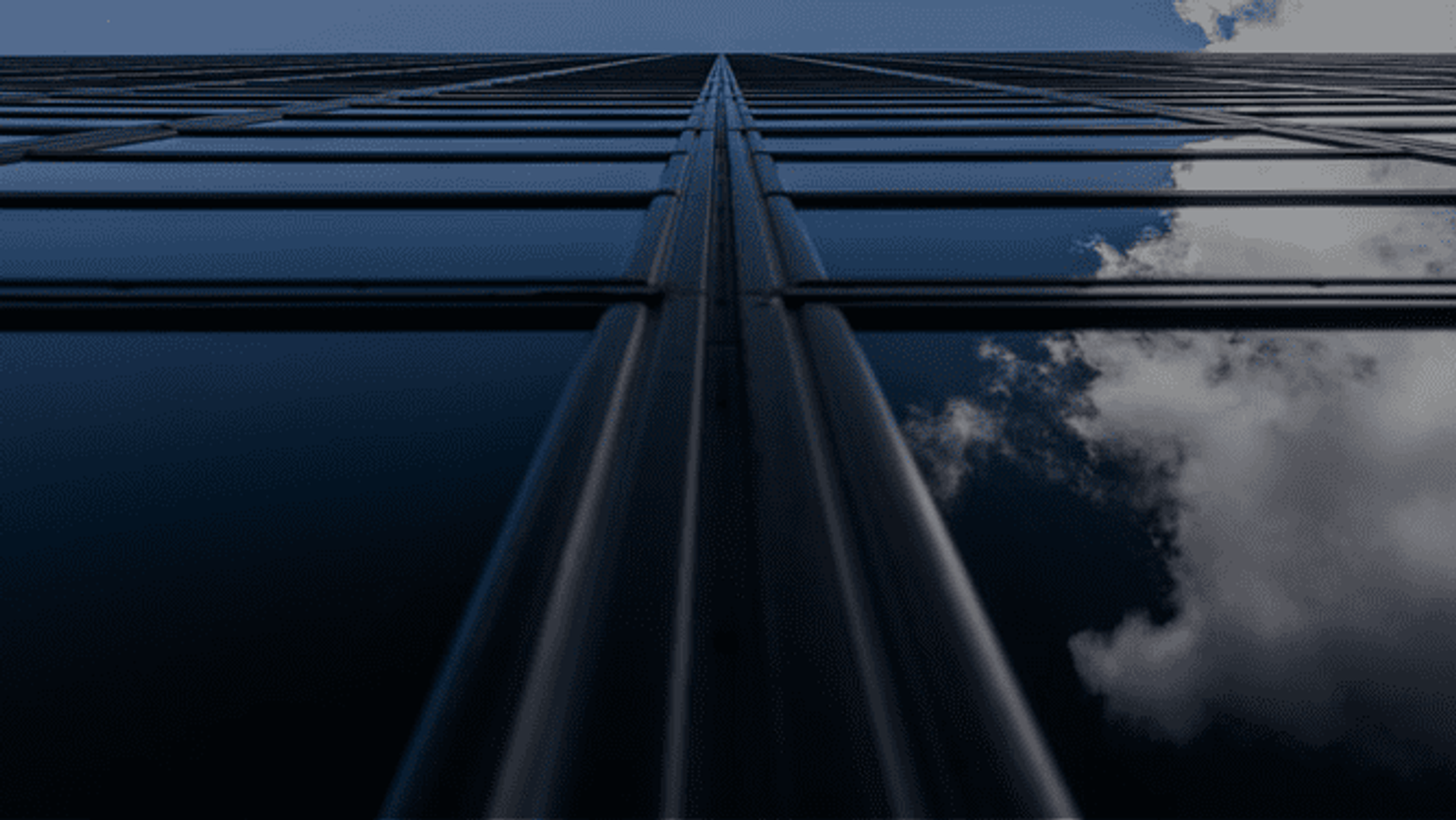 looking up at a tall building with clouds reflected in the windows