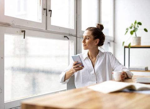 a woman is sitting at a table with a cup of coffee and a cell phone .