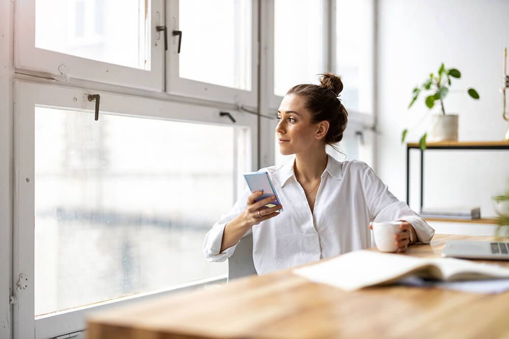 a woman is sitting at a table with a cup of coffee and a cell phone .