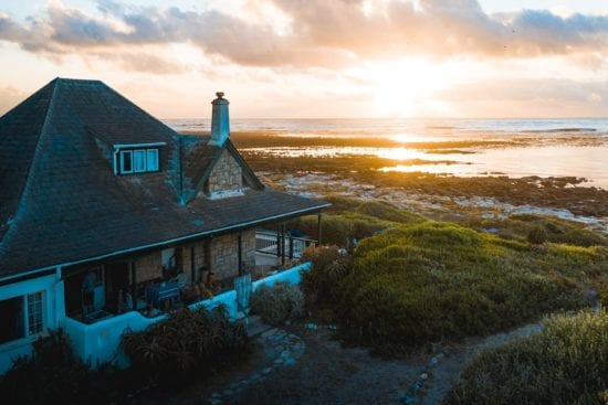 an aerial view of a house on a hill overlooking the ocean at sunset .