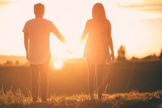 a man and a woman are holding hands in a field at sunset .