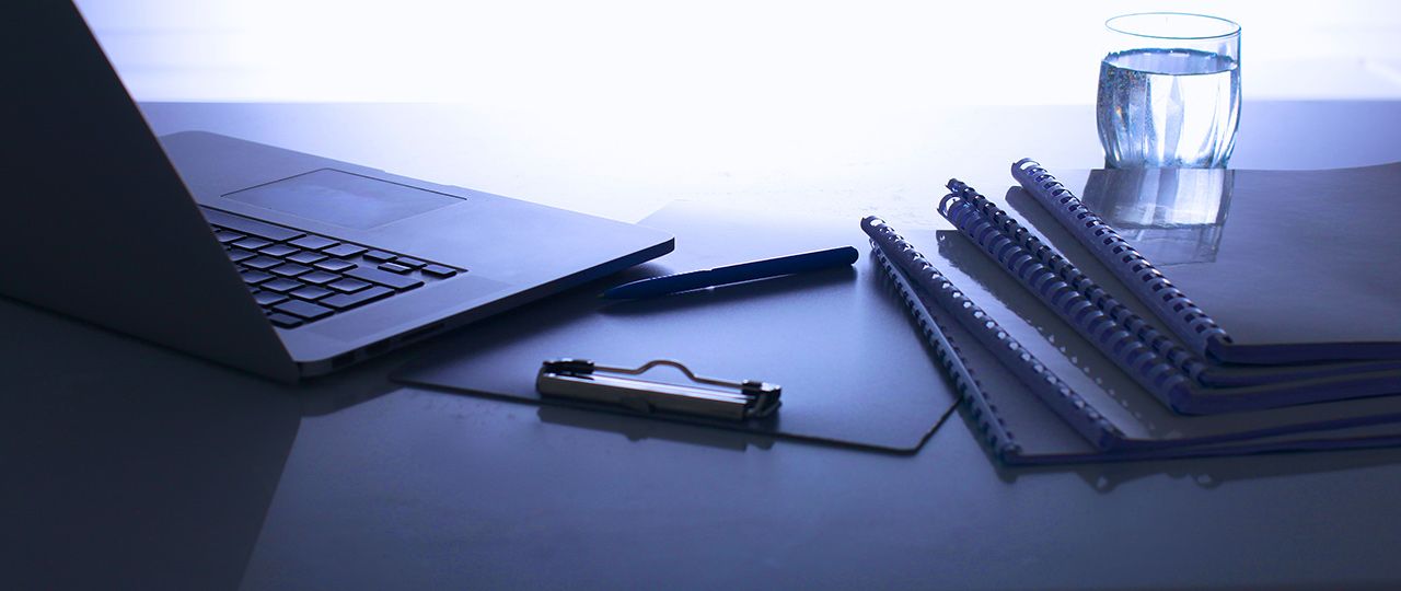a laptop , notebooks , a pen , and a glass of water are on a desk .