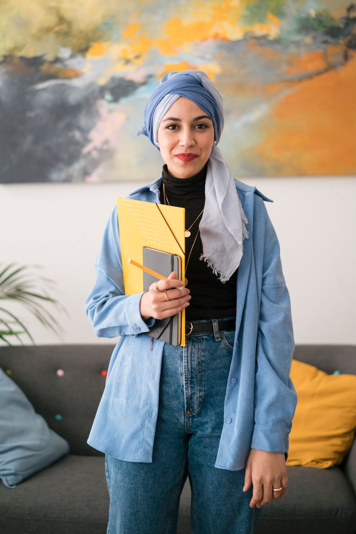 a woman in a hijab is holding a notebook and a pencil .