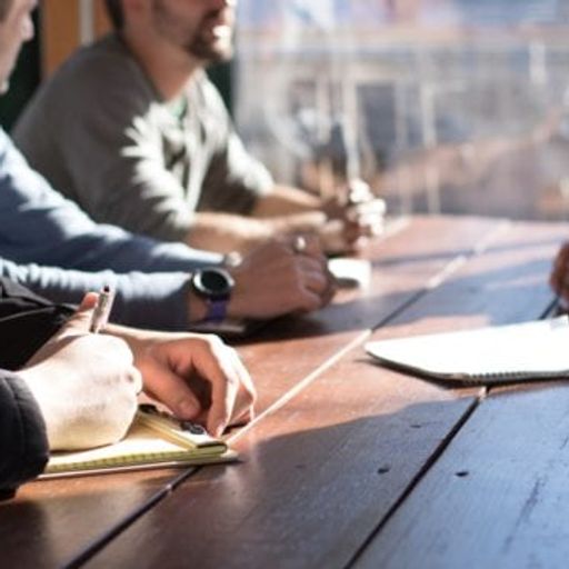a group of men are sitting at a wooden table having a meeting .