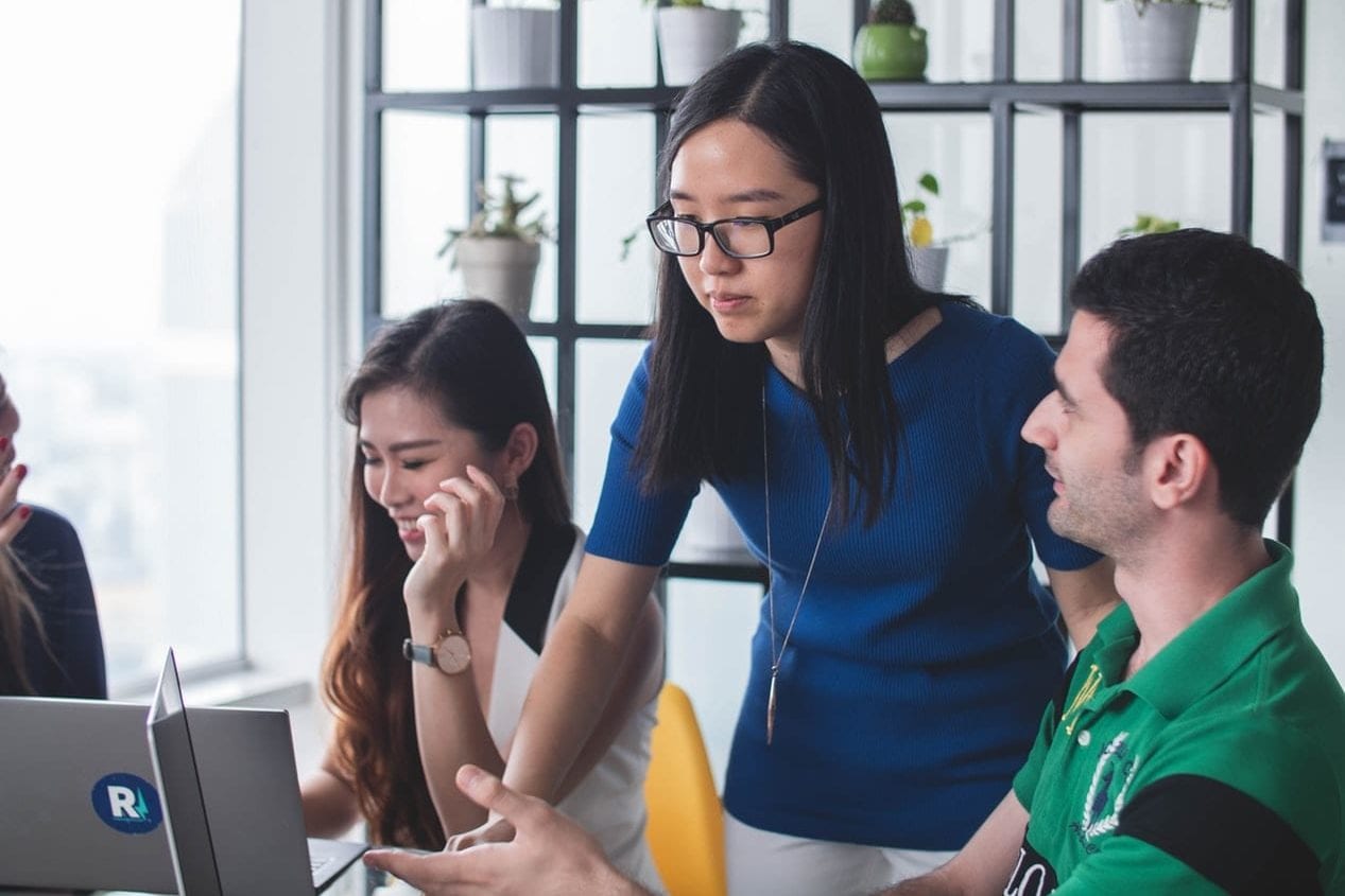 a group of people are sitting around a table looking at a laptop computer .