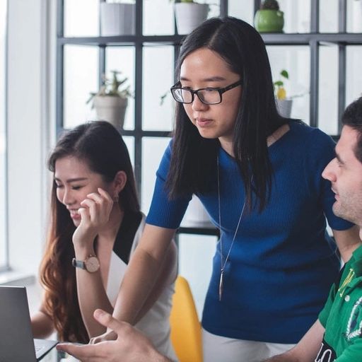 a group of people are sitting around a table looking at a laptop computer .