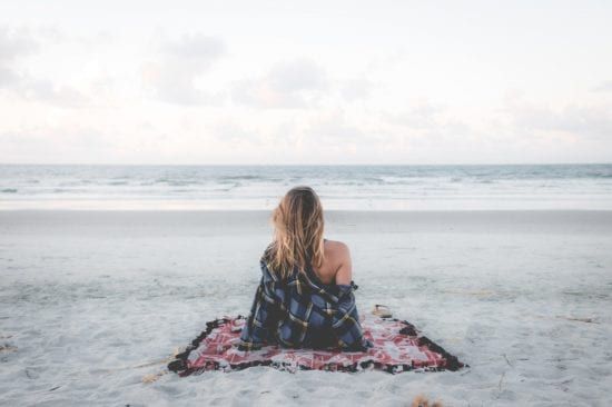 a woman is sitting on a blanket on the beach looking at the ocean .
