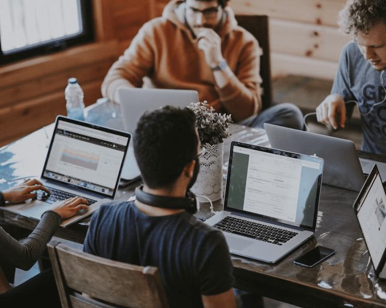 Four people work on laptops around a wooden table.