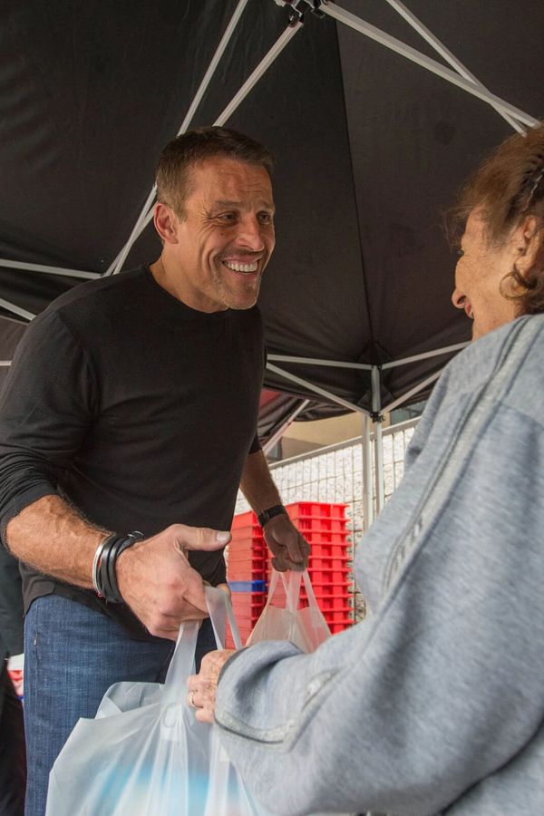 Five smiling people, one man and four women, pose outdoors under blue tents; three women wear black "BEY GOOD" shirts.