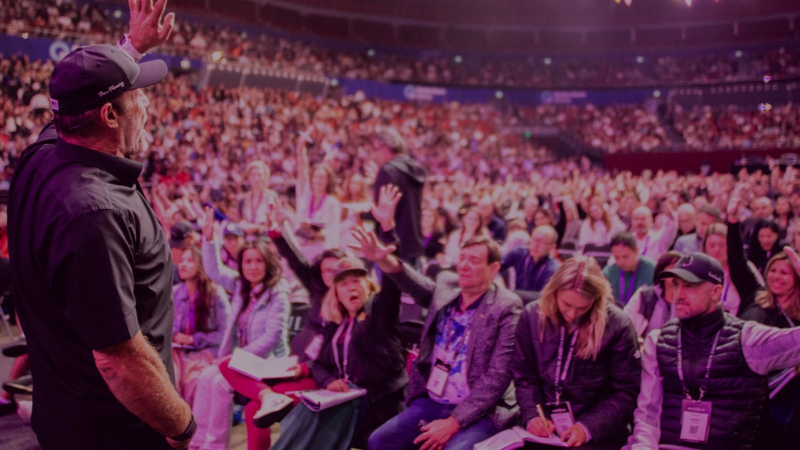 a man is standing in front of a crowd of people raising their hands in the air .