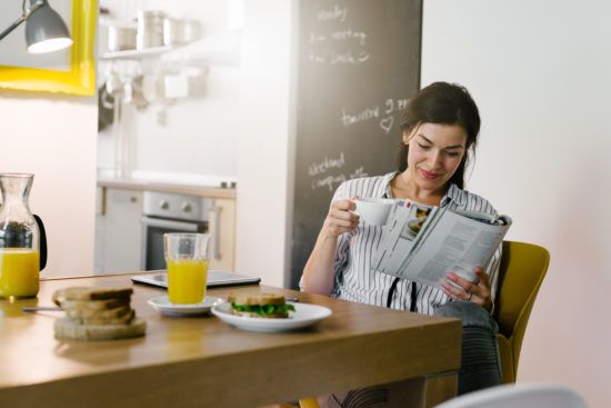 a woman is sitting at a table drinking coffee and reading a newspaper .