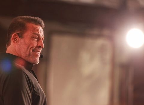Tony Robbins smiling and wearing a headset microphone, with a bright light in the background.