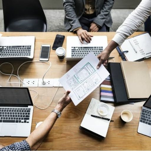 a group of people are sitting around a table with laptops and papers .