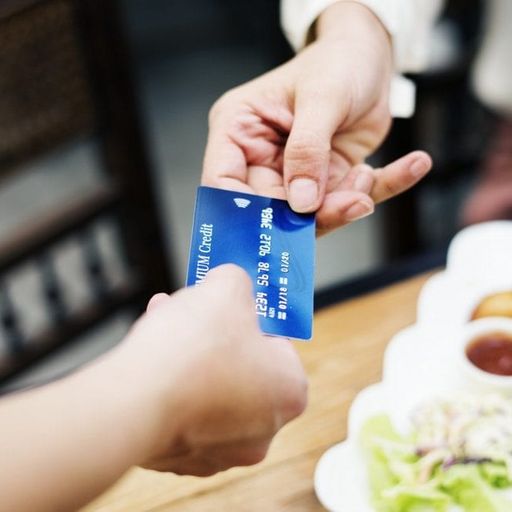 a person is handing a credit card to another person in front of a plate of food .