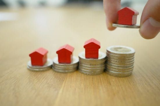 a person is putting a red house on top of a stack of coins .