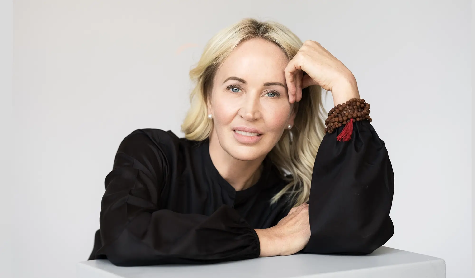 A smiling blonde woman with a microphone claps, surrounded by warm lens flares.
