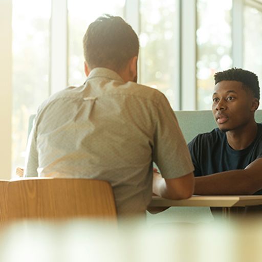 two men are sitting at a table having a conversation .