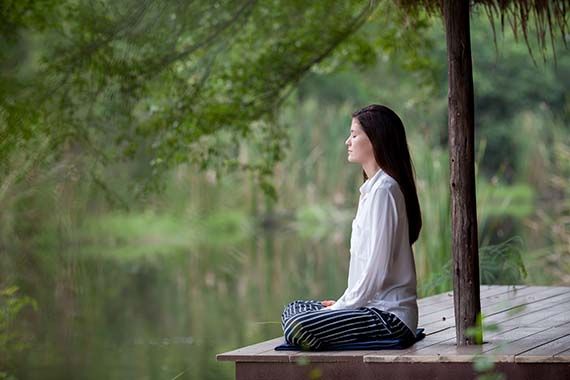 a woman is sitting on a wooden dock with her eyes closed .