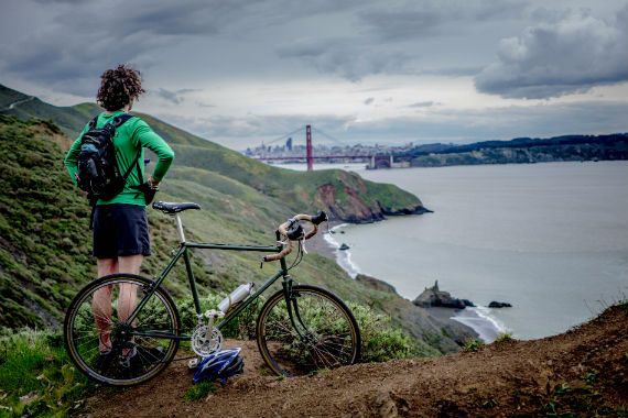 a man is standing next to a bicycle on a hill overlooking the golden gate bridge .