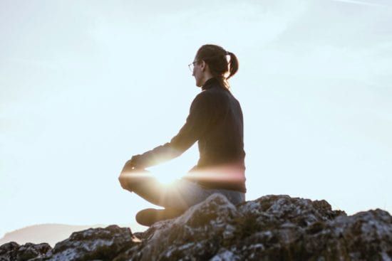 a woman is sitting in a lotus position on top of a rocky hill .