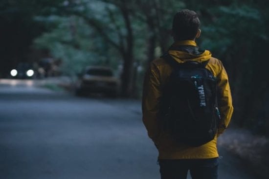 a man with a backpack is walking down a road at night .
