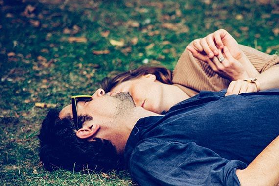 a man and a woman are laying on the grass holding hands .