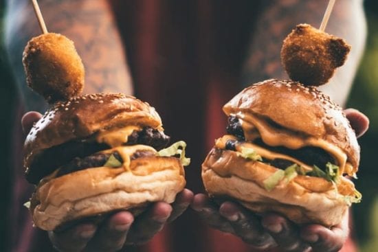 a person is holding two hamburgers in their hands .