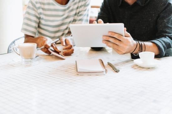 two people are sitting at a table looking at a tablet .