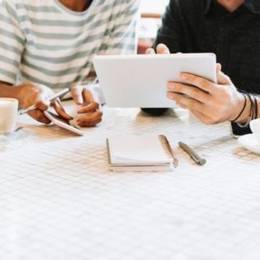 two people are sitting at a table looking at a tablet .