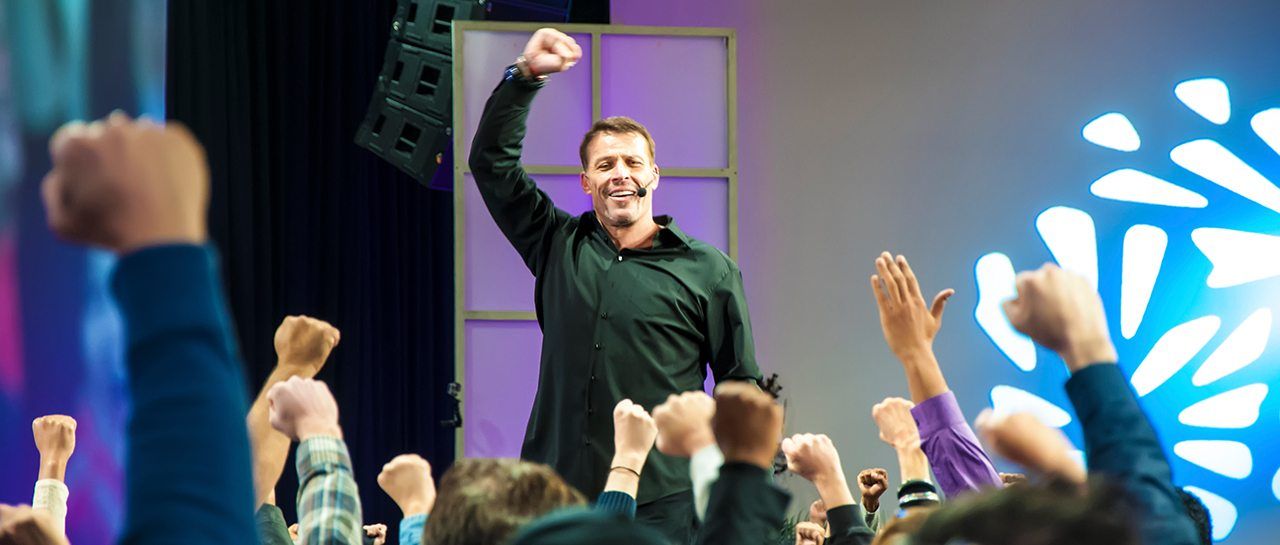 a man is standing on a stage in front of a crowd of people with their hands in the air .