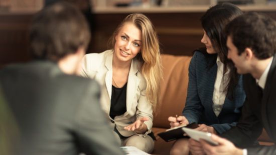 a group of business people are sitting around a table having a meeting .